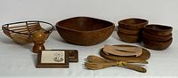 Photo shows the entire lot including large wooden salad bowl, six small wooden bowls stacked, wooden artisan cheese board with spreader, serving forks tied with string, wooden salt/pepper mill, and two retro-style trivets made from wooden strips and black wire.