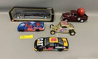 Five model cars laid out on table, including boxed black Lincoln limousine, burgundy Chevrolet pickup with apple in bed, and three race cars.