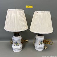 Pair of vintage ceramic table lamps with white pleated shades side by side on gray background