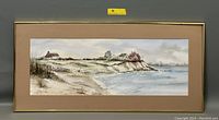 Full view of the framed watercolor painting depicting a beachside cliff with houses and a sandy shore, showing the artwork size and presentation.