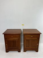 Front view of the pair of cherry wood nightstand cabinets, showing drawer and door with wooden knobs