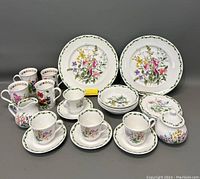 Full set of floral pattern dinnerware items including mugs, teacups, saucers, plates, bowls, sugar bowl and creamer arranged on table.