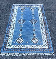 Top-down view of the entire rectangular denim blue Turkish Kilim area rug laid flat on pavement, showing overall geometric pattern and fringe edges.