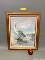 Full view of the gilt gold framed oil painting showing a lighthouse overlooking a beach landscape with dune grasses and ocean.