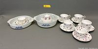 Wide shot of all items in the lot: three milk glass serving bowls, white ceramic teapot with floral design, and six assorted porcelain tea cups with saucers.