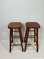 Front view of two vintage wooden bar stools placed side by side against white background.