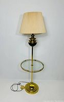 Full view of vintage brass floor lamp with pleated cream shade, circular glass tray and brass base with cord visible