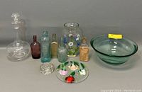 Wide shot of all glass items including decanter, medicine bottles, flower frog, bowl, vase, and art plate.