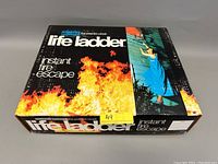 Photo of the original Life Ladder box featuring fire imagery and a person escaping a window, emphasizing the product's use as a fire escape ladder.