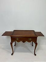 Front view of vintage tea table with extended pull out trays on either side, showing the cabriole legs and drawer with brass handles.