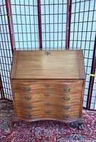 Front view of the vintage wooden slant front desk with claw feet showing the four drawers and curved shape.