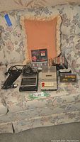 Overview of the lot including 2 vintage cassette recorders, microphone, battery charger, multiple cassette tapes and cases, all placed on a floral couch.