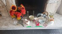 Wide view of all items showing artificial sunflowers, red flowers, two glass vases, duck figurine, striped mug, pastel floral cup, ceramic soap dishes, basket dish, and vintage mirror
