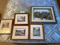 Lot layout showing four framed prints and one larger framed paper tole piece on mattress surface.