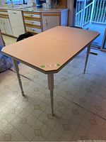 Angled side view of white kitchen table showing turned wooden legs and arborite top with bevel edges and corner angle.