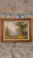 Framed landscape painting depicting a forest and lake with a gold wooden frame, measuring 16x21 inches.