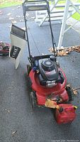 Front view of the Toro red mower showing collector bag and attached gas jugs on pavement with some leaf debris