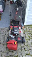 Front-top view showing the black fabric grass collection bag, control handle, and front deck of the mower with red accents.