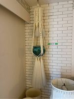 Full view of macrame hanger holding the ceramic pot against a wall, showing length and structure.