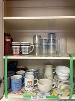 Cupboard shelf with assorted mugs, clear drinking glasses, small bowls, and an ironstone cream and sugar set.