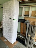 Twin size white quilted mattress standing vertically next to wall and wooden ladder