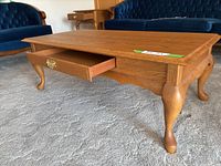 Side view showing oak coffee table, drawer slightly open with brass handle, curved legs.