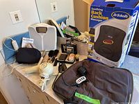Overview of personal care items on a blue table, showing the Dr Scholl's back cushion massager box, digital scale, hair dryer, and various small items.