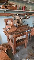 Radial arm saw mounted on homemade wooden bench with surrounding workshop environment visible.