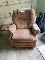 Front view of a large brown fabric recliner chair with padded arms and button tufted backrest, showing upholstery and overall shape.