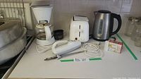 Photo showing entire lot of small appliances including coffee maker, toaster, kettle, electric cutting utensil, white extension cord, and box of heating elements.