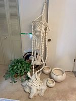 Full view of the macrame hanger with ceramic pots and artificial plant beside it.