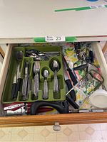 Full view of the kitchen drawer showing green cutlery tray with knives, forks, spoons, and assorted kitchen tools to the side.