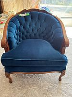 Front view of royal blue upholstered vintage Victorian style chair with tufted backrest, wooden frame carved with scroll details, and plush seat cushion.