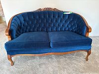 Front view of blue velvet loveseat with carved wood frame and button tufted back
