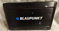 Top view of black Blaupunkt AMP2002 power amplifier showing logo, model and some wear and scratches.