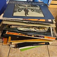 Stack of assorted vintage vinyl records with various album covers visible, showing wear and edge damage.
