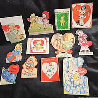Overhead photo showing the first group of vintage Valentine’s Day cards arranged on black fabric, displaying various character and heart themed cards.