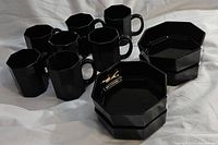 Six black octagonal mugs and four matching black octagonal bowls arranged on a surface