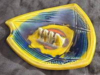 Top view showing triangular shape, yellow glaze with blue and red abstract design and imperfections