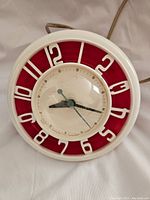 Front view of the mid century electric clock showing round shape, red and white color scheme, and clock hands under a circular glass cover.