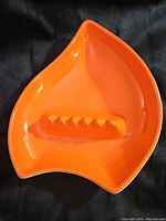 Top view of the orange pottery ashtray showing its distinctive curved triangular shape with cigarette rests in the center.