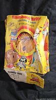 Damaged yellow box labeled Rainbow Brite Costume & Mask by Collegeville, with a window showing part of the costume inside and artwork of Rainbow Brite and friends.