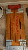 Top view of the closed wooden mechanics creeper with Snap-on red logo and metal corner reinforcements, showing overall well-kept condition.