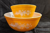 Both large and small vintage Pyrex mixing bowls stacked, showing bright yellow color and white Butterfly Gold floral pattern.