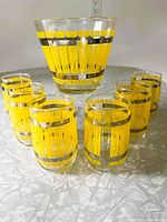 Photo showing six vintage barrel-themed glasses with yellow and silver banding arranged in arc with matching barrel-shaped ice bucket behind.