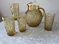 Set of one Honey Gold / Amber textured glass pitcher with handle and spout, and four matching tumblers on tabletop