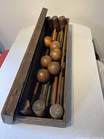 Croquet set inside original wooden storage box with lid open showing mallets and balls inside.