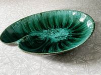Oblique side view showing the glossy green ceramic surface and the bowl's unique curved shape.