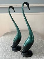 Photo showing both Blue Mountain Pottery swan figurines side by side on a table, illustrating their tall, slender shapes and blue-green colors.