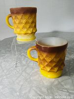 Two Fire King Anchor Hocking Kimberley mugs in yellow and brown ombre with diamond texture pattern on display stands